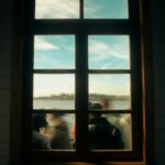 Window view showing blurred silhouettes of people and a scenic water landscape.