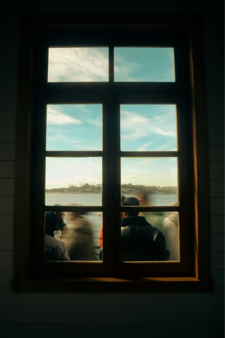 Window view showing blurred silhouettes of people and a scenic water landscape.