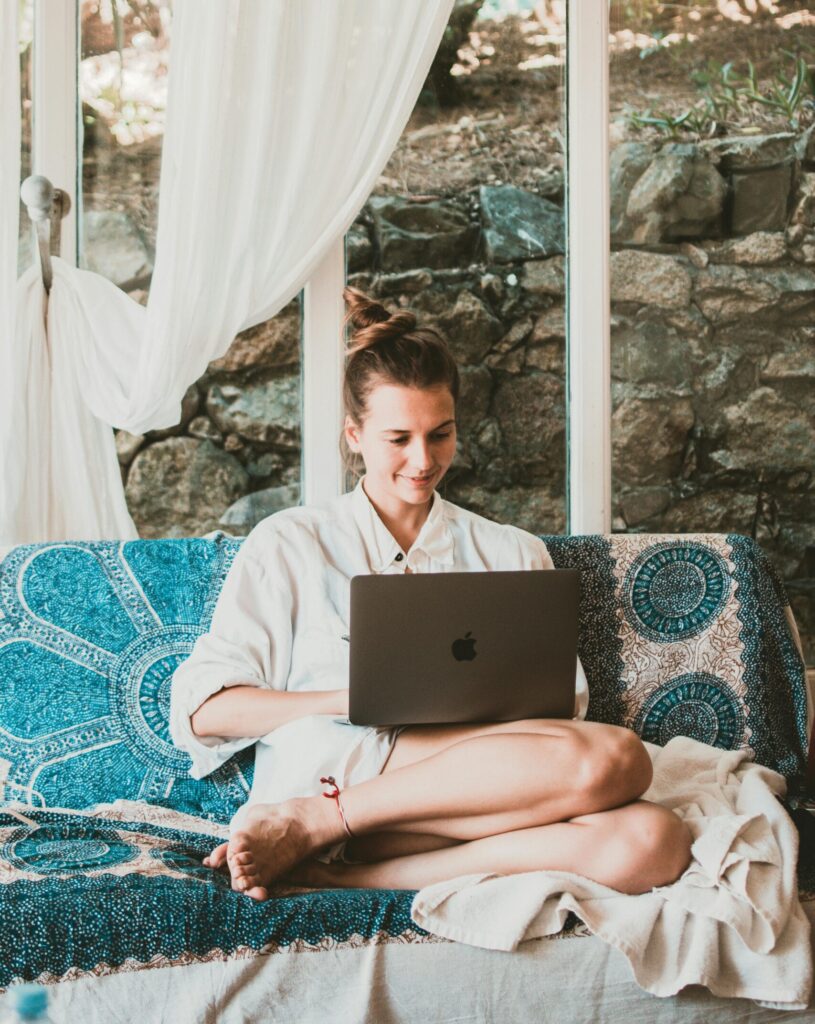 A woman sitting comfortably on a sofa using a laptop, depicting a serene remote work setup.